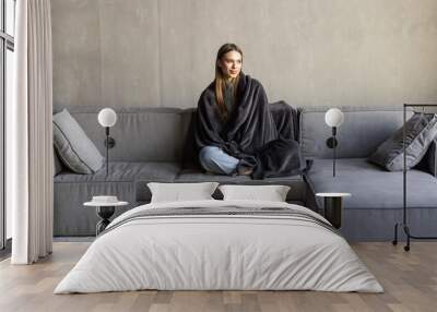 cutewoman relaxing o the sofa wrapped in a soft grey blanket Wall mural